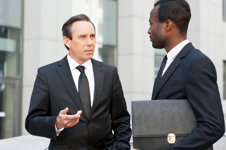 Two confident business men talking and gesturing while standing outdoors