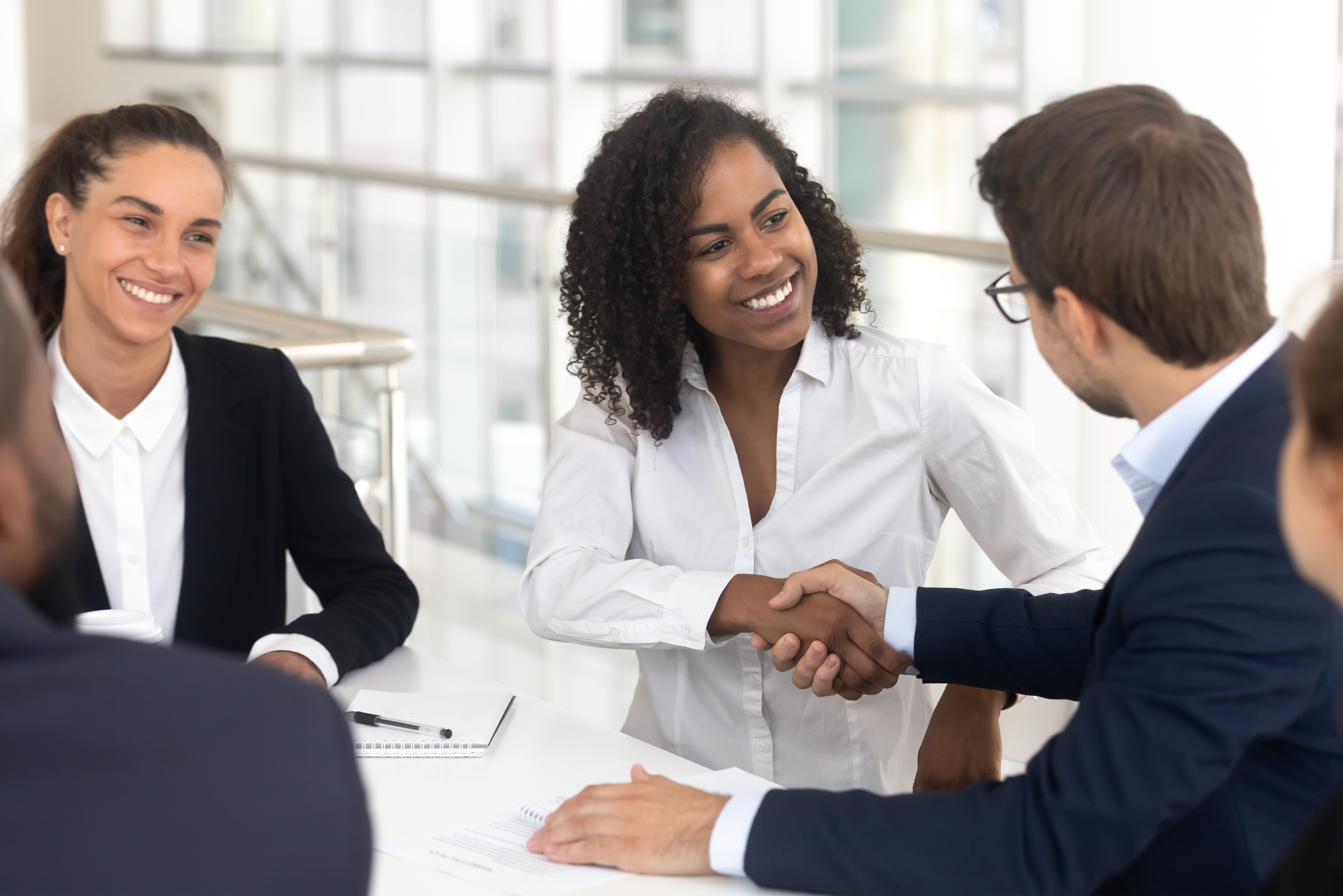 Multiracial businessman businesswoman shake hands starting collaboration at group negotiations.
