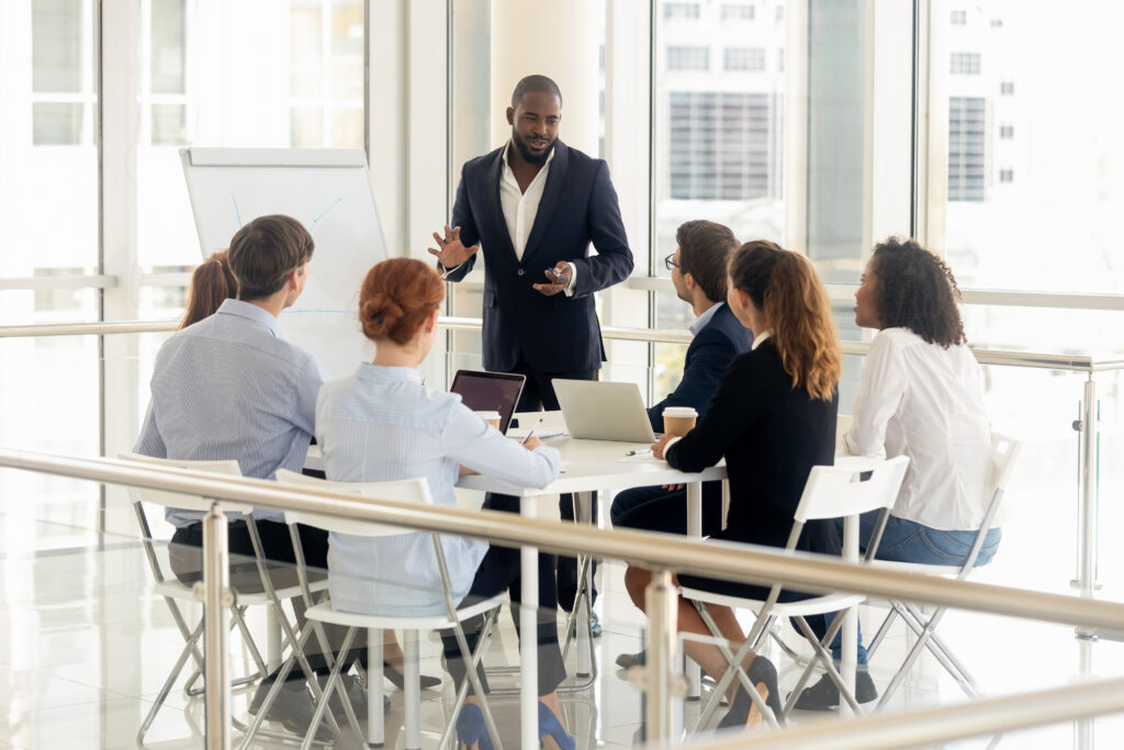 Smiling african American businessman stand make flip chart presentation for diverse work team in office