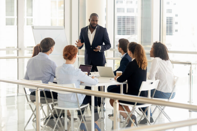 Smiling african American businessman stand make flip chart presentation for diverse work team in office
